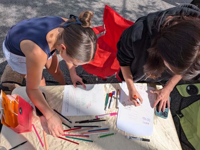 Two neighbors writing messages for the time capsule at an outdoor table